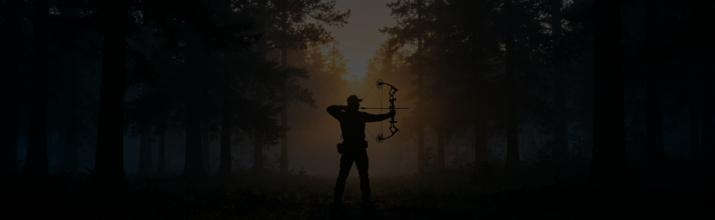Archer at full draw silhouetted against a forest at dawn